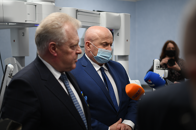 Dwóch mężczyzn stoi w sali medycznej przed nimi dziennikarze trzymają mikrofony