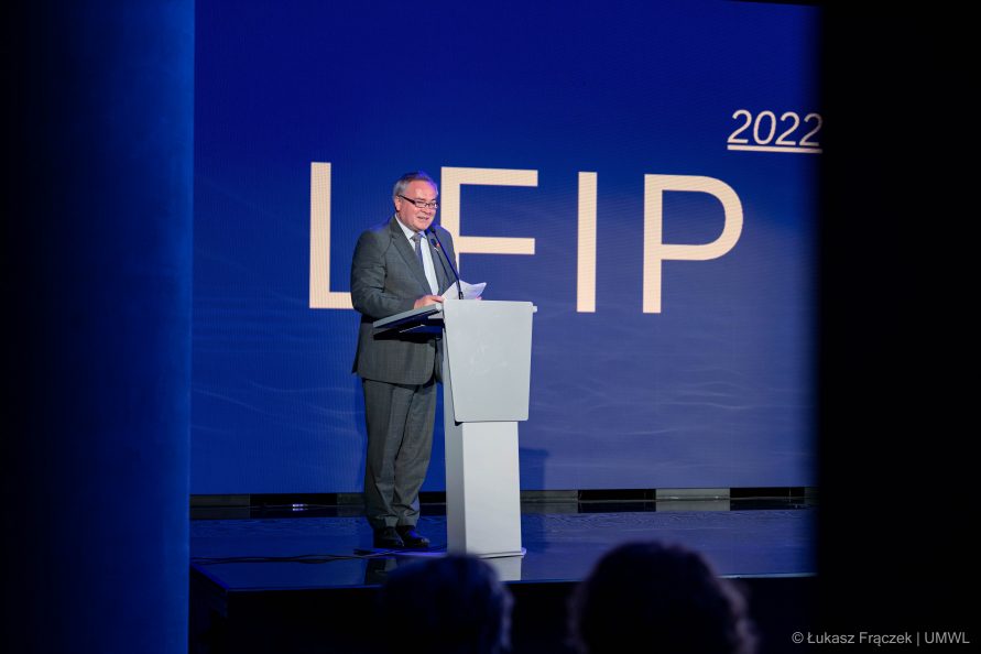 Mężczyzna stoi przy mównicy podczas przemówienia na niebieskim tle z napisem "LFIP 2022"