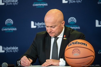 Marszałek Jarosław Stawiarski siedzi i przy stole i podpisuje odkument. na pierwszym planie przed nim leży piłka do koszykówki