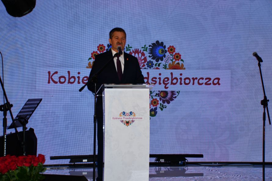 Członek Zarządu Zdzisław Szwed stoi przy mównicy, za nim na ekranie wyświetla się duży napis Kobieta Przedsiębiorcza