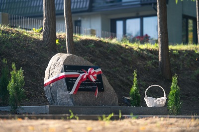 Widok na kamień z tablicą pamiątkową owinięta biało czerwoną wstęga