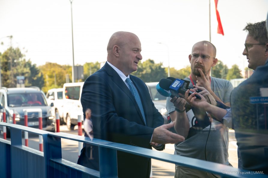 Marszałek Jarosła Stawiarski stoi na zewnątrz przed budynkiem szpitala i odpowiada na pytania dwóch dziennikarzy