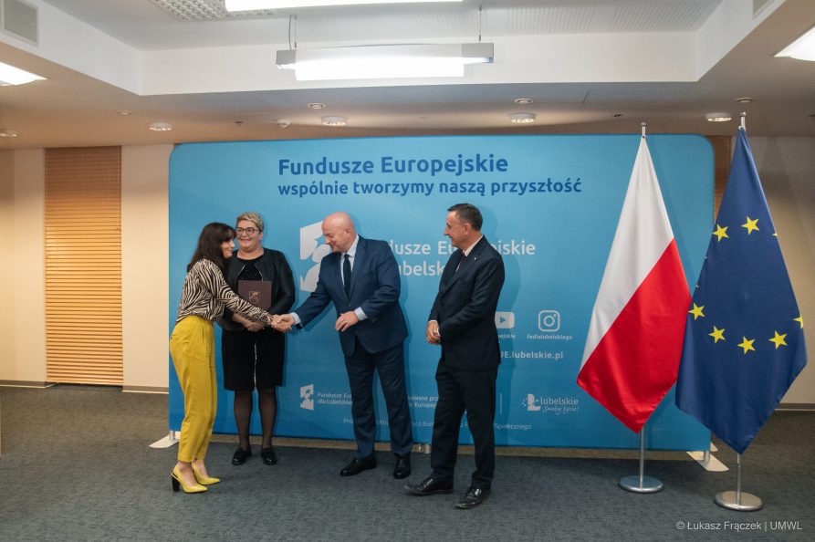 Dwie kobiety i dwóch mężczyzn. W tym gronie marszałek Jarosław Stawiarski podaje rękę jednej z kobiet. Za nimi znajduje się ścianka z napisem Fundusze Europejskie