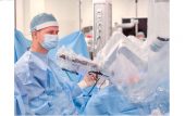 Chirurg w fartuchu stoi przy stole operacyjnym i trzyma w ręce sprzęt chirurgiczny