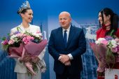 Dwie młode kobiety, jedna w koornie Miss Polonia pozują do zjdęcia z Marszałkiem Jarosławem Stawiarskim. Obie trzymają w rękach bukiety kwiatów