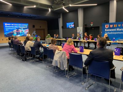 Kilkadziesiąt osób siedzi na sali konferencyjnej na przedzie sali jest ustawiony duży ekran, który wyświetla prezentację