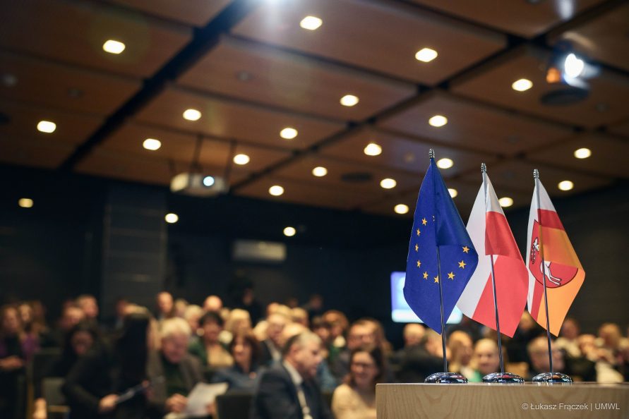 Na stole znajdują się trzy flagietki województwa lubelskiego, polski i unii europejskiej