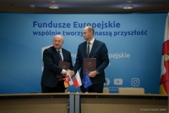 Marszałek Województwa Lubelskiego w geście gratulacyjnym podaje rękę jednemu z beneficjentów programu. Mężczyzna trzyma w drugiej ręce teczkę z dokumentami