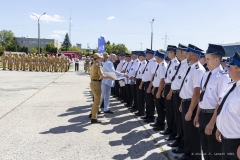 Na placu w słoneczny dzień stoi grupa strażaków ustawiona w rzędzie. Marszałek województwa lubelskiego podchodzi do każdego i podaje rękę