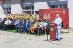 Marszałek województwa lubelskiego stoi przy mównicy ustawionej na zewnątrz przed budynkiem. Za nim na krzesłach siedzi około dwudziestu uczestników wydarzenia