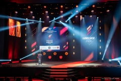 Marszałek Jarosław Stawiarski stoi na scenie, za nim w tle na wielkoformatowym ekranie wyświetla się grafika dotycząca  olimpiady