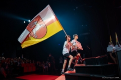 Dwóch chłopców wchodzi po schodach na scenę, jeden z nich trzyma flagę województwa lubelskiego a drugi trzyma plansze z napisem województwo lubelskiego