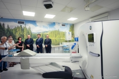 Trzech mężczyzn i cztery kobiety w tym trzy pielęgniarki stoją w pomieszczeniu medycznym, na pierwszym planie znajduje się tomograf