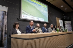 Wicemarszałek Marek Wojciechowski w towarzystwie kilku innych osób siedzi przy długim stole podczas konferencji prasowej.