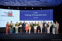 Na scenie pozuje wspólnie kilkunastu laureatów certyfikatu, za nimi na dużym ekranie wyświetla się napis Gala Zakup  Prospołeczny 2024