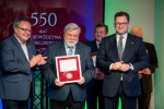 Dwóch członków zarządu województwa lubelskiego pozuje do zdjęcia w laureatem medalu zasłużony dla województwa lubelskiego.